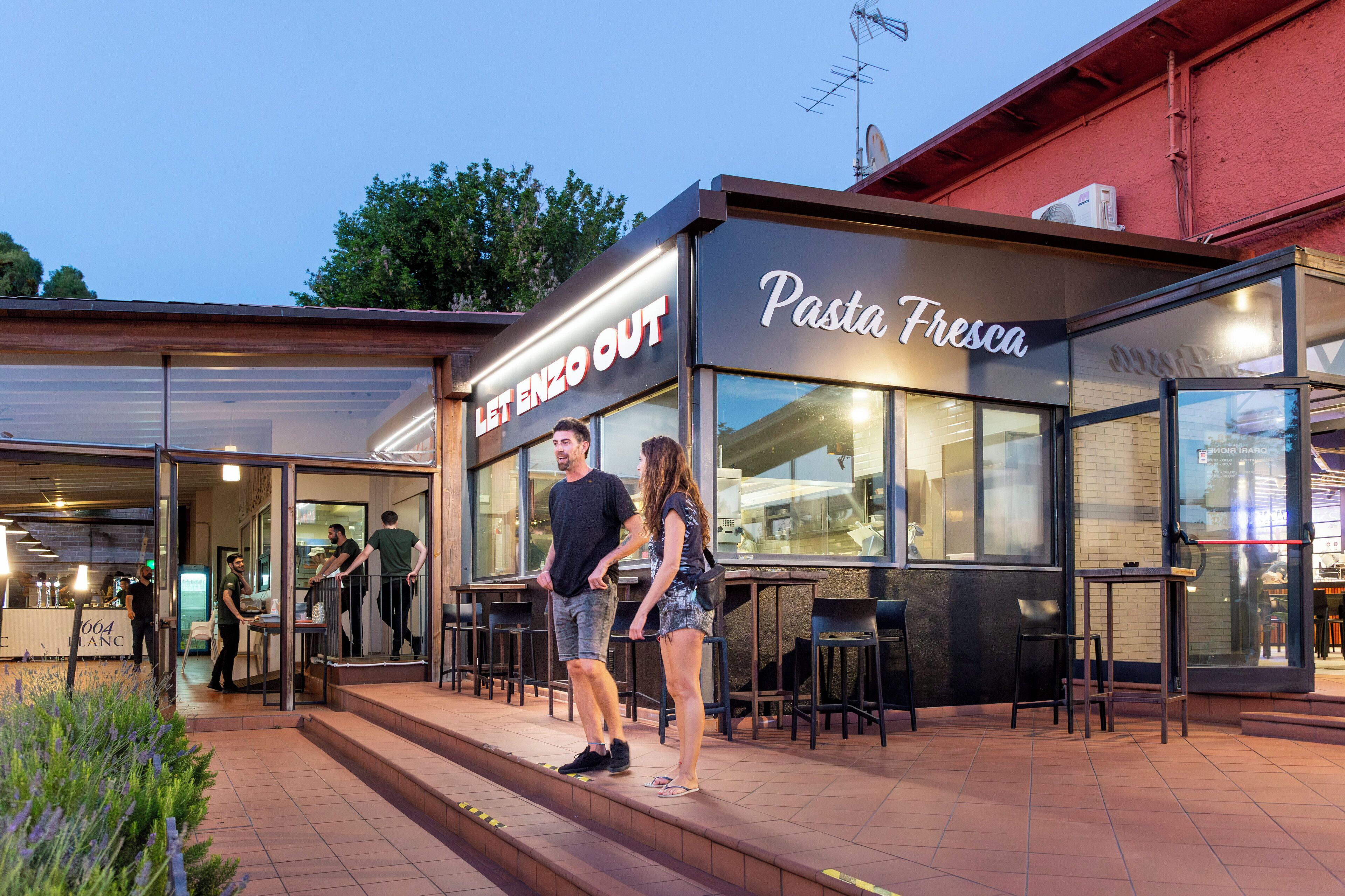 Ein Außenbereich eines Restaurants mit einem Schild, auf dem 'Let Enzo Out' und 'Pasta Fresca' steht.