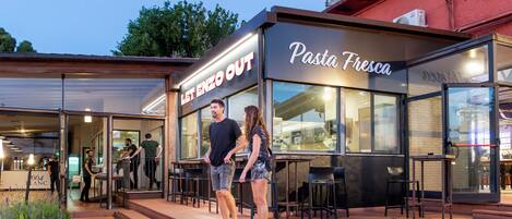An outdoor seating area of a restaurant with a sign reading "Let Enzo Out" and "Pasta Fresca."
