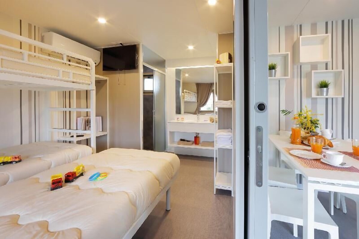 Una habitación de hotel con literas, un comedor con desayuno y un baño con espejo y estantes.