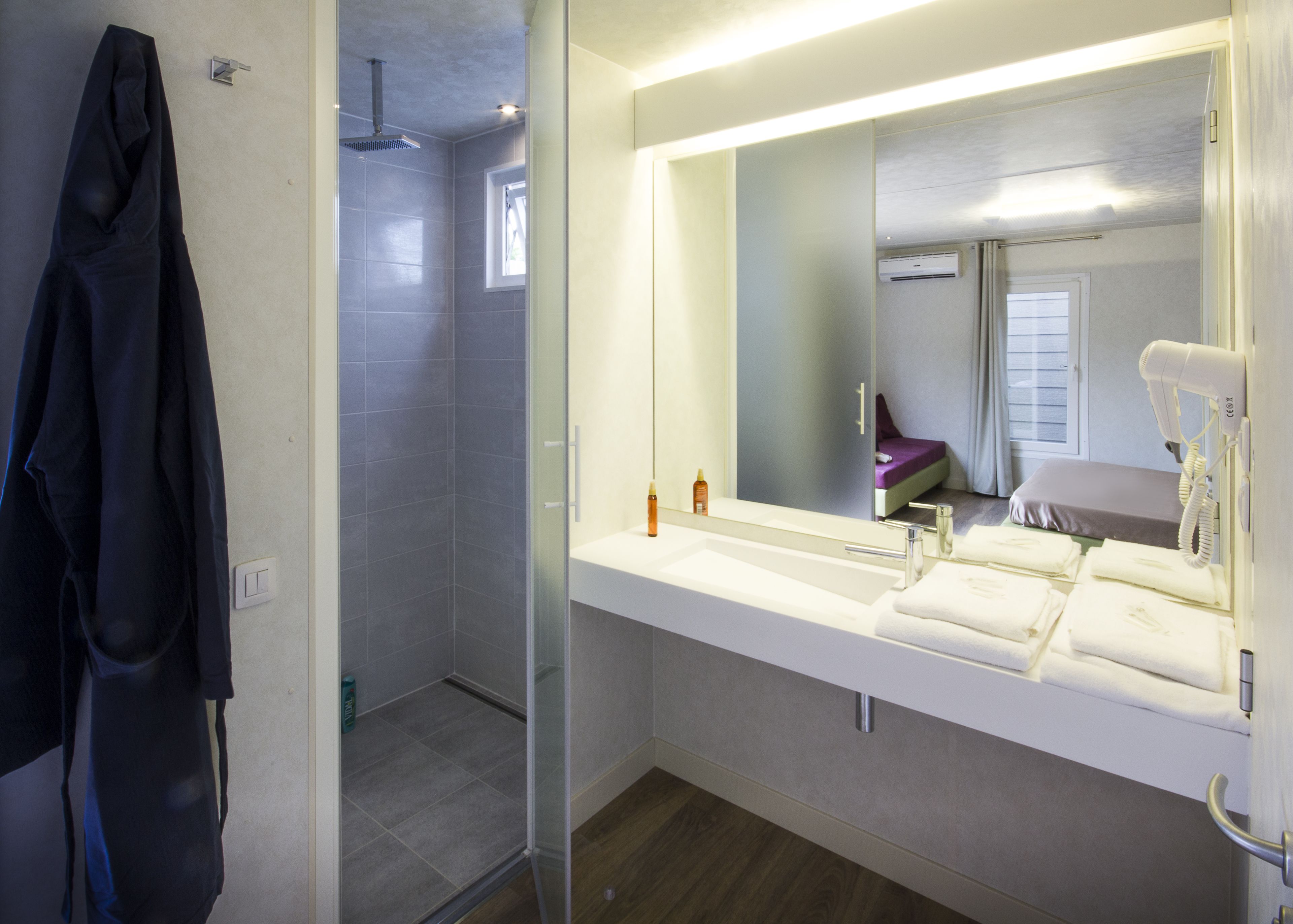 A modern bathroom with a glass-enclosed shower, a large mirror, and a vanity with a sink and towel rack.