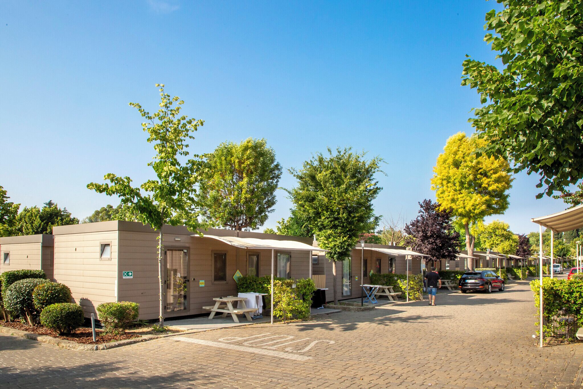 A row of mobile homes with outdoor seating areas and a paved parking area.