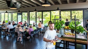 A restaurant with large windows, wooden floors, and a buffet counter with fruits and vegetables.
