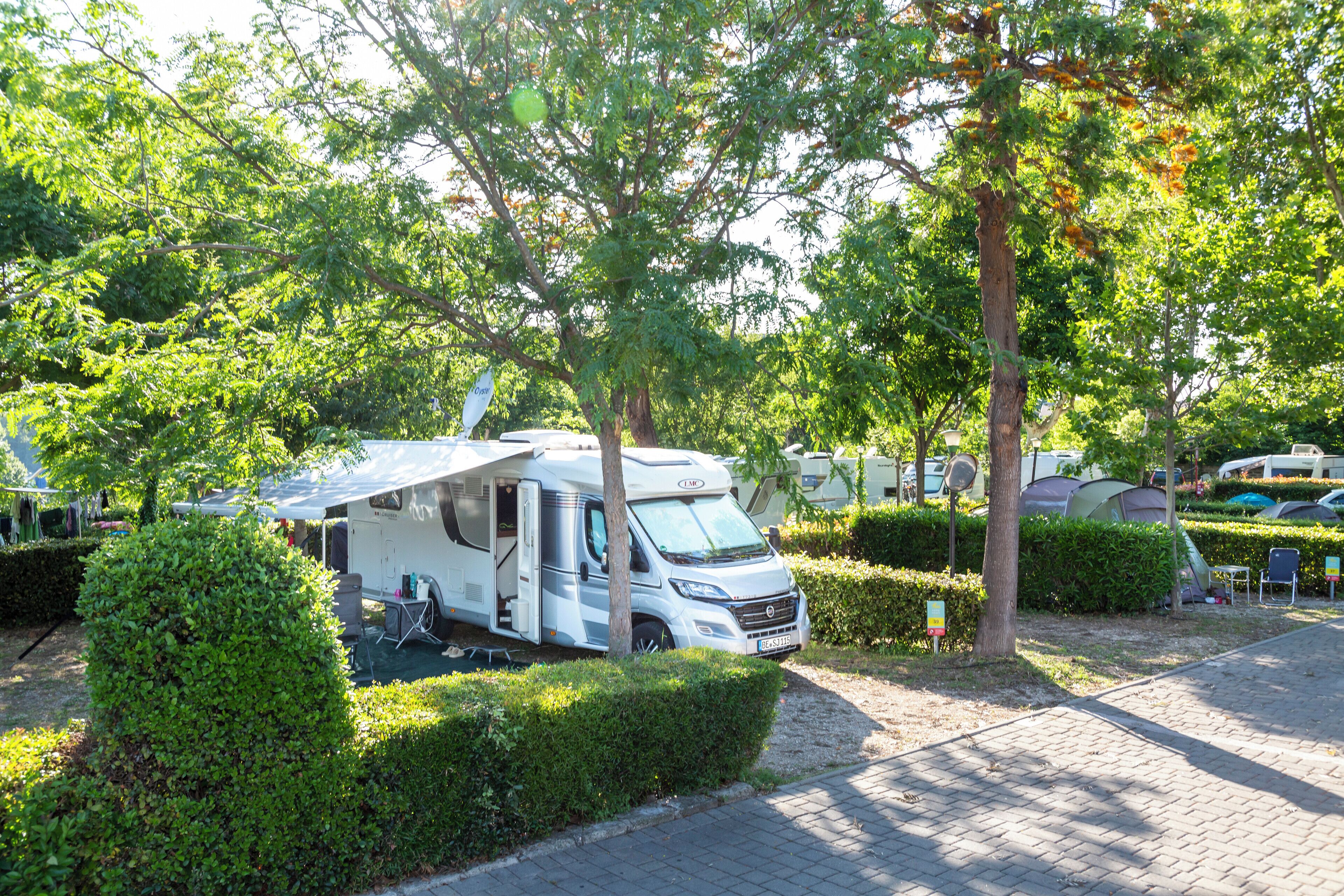 Une caravane est stationnée dans un terrain de camping, entourée d’arbres et de verdure.
