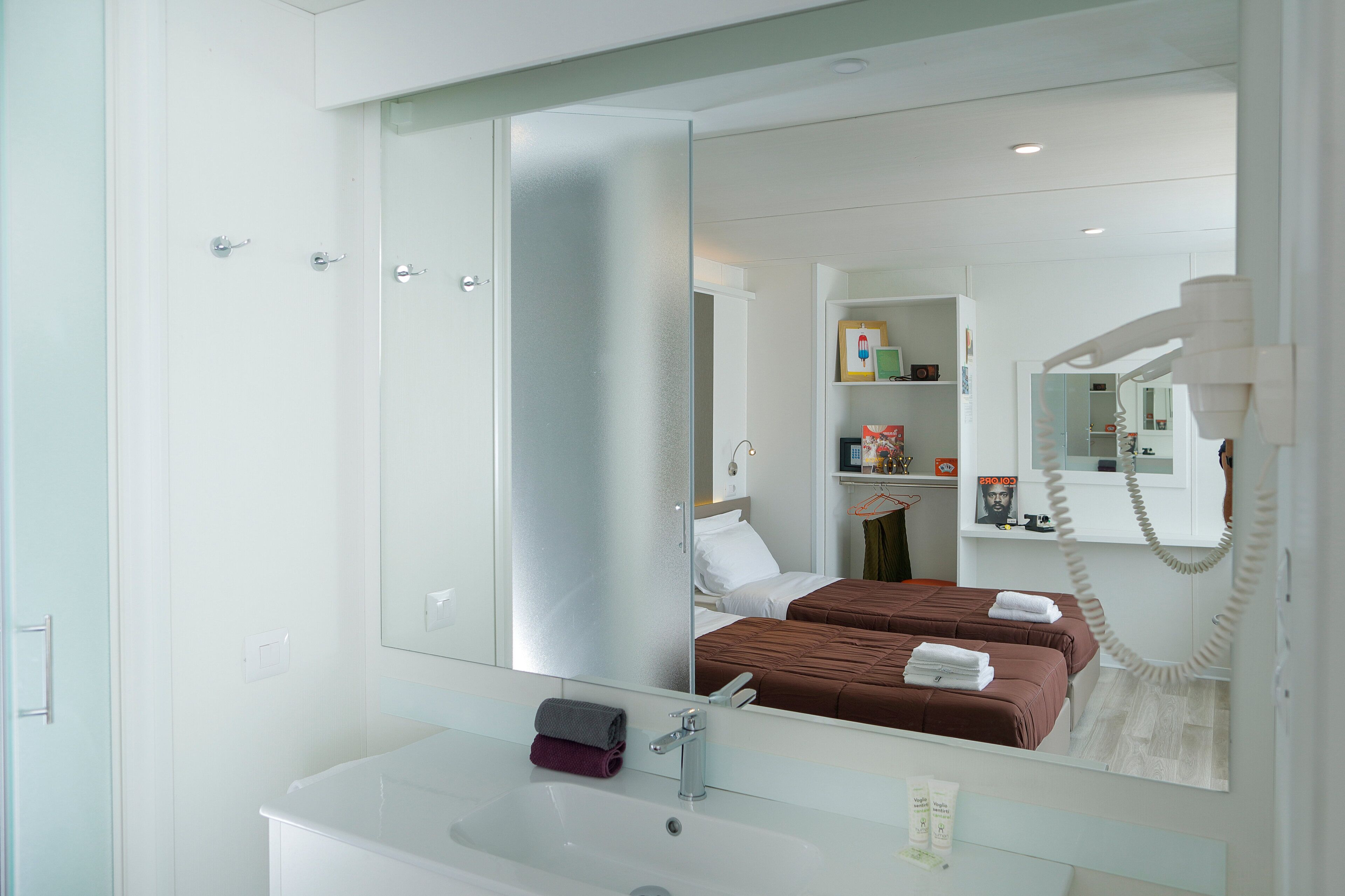 A modern bathroom with a large mirror, a white sink, and a bed with brown bedding.