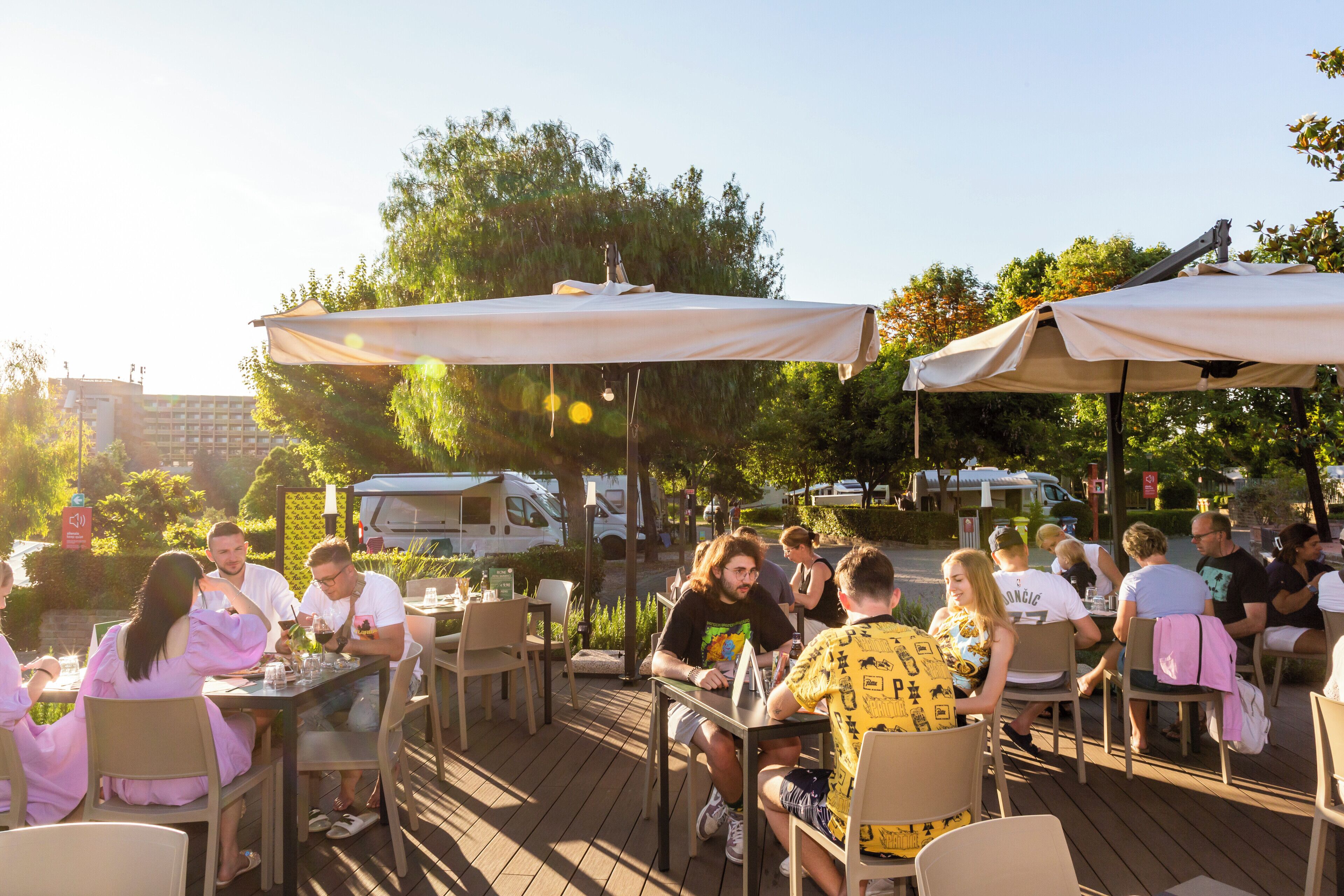 An outdoor dining area with tables and chairs, umbrellas, and people dining.