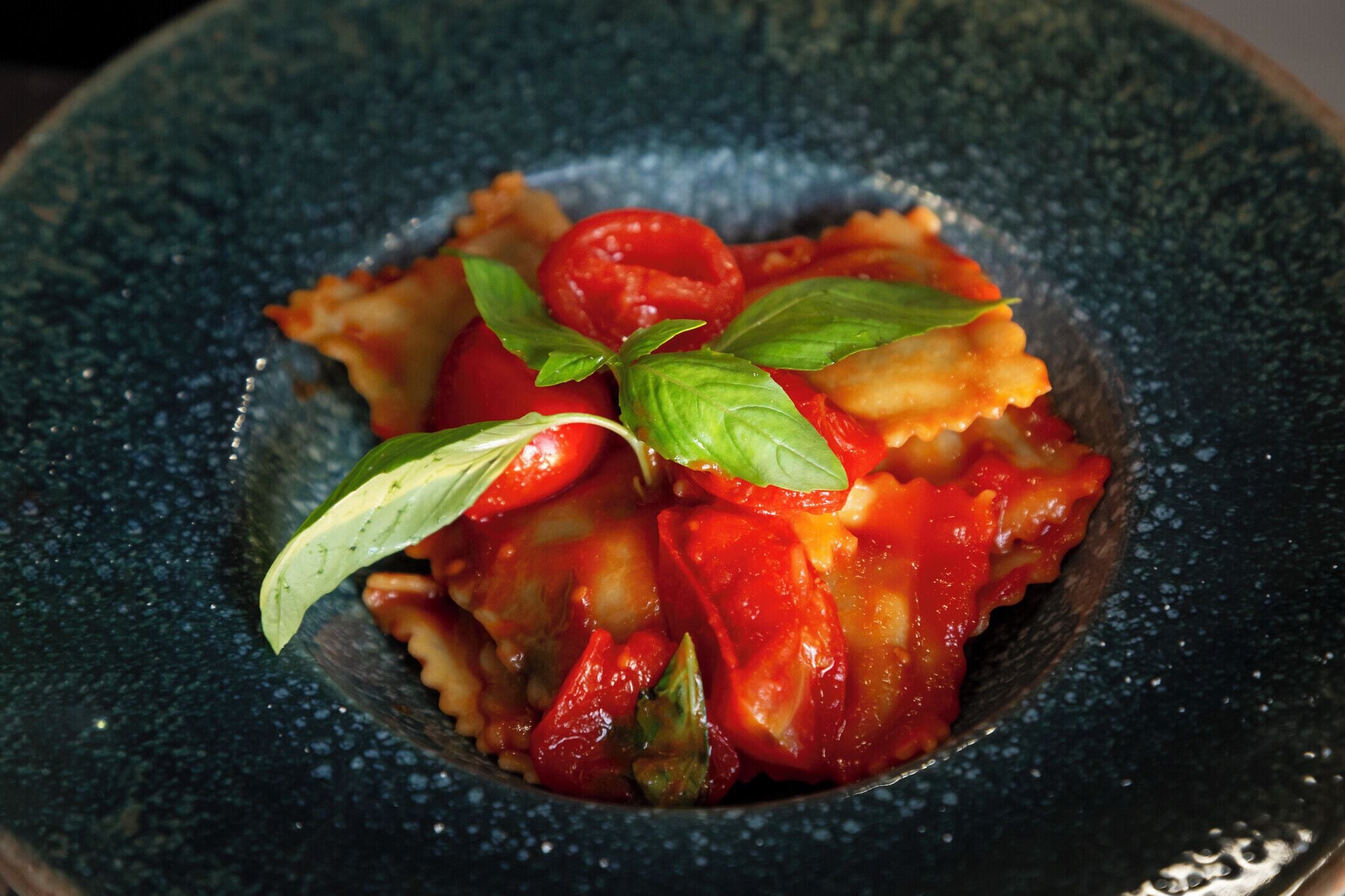 Un bol de raviolis à la sauce tomate, garni de feuilles de basilic.