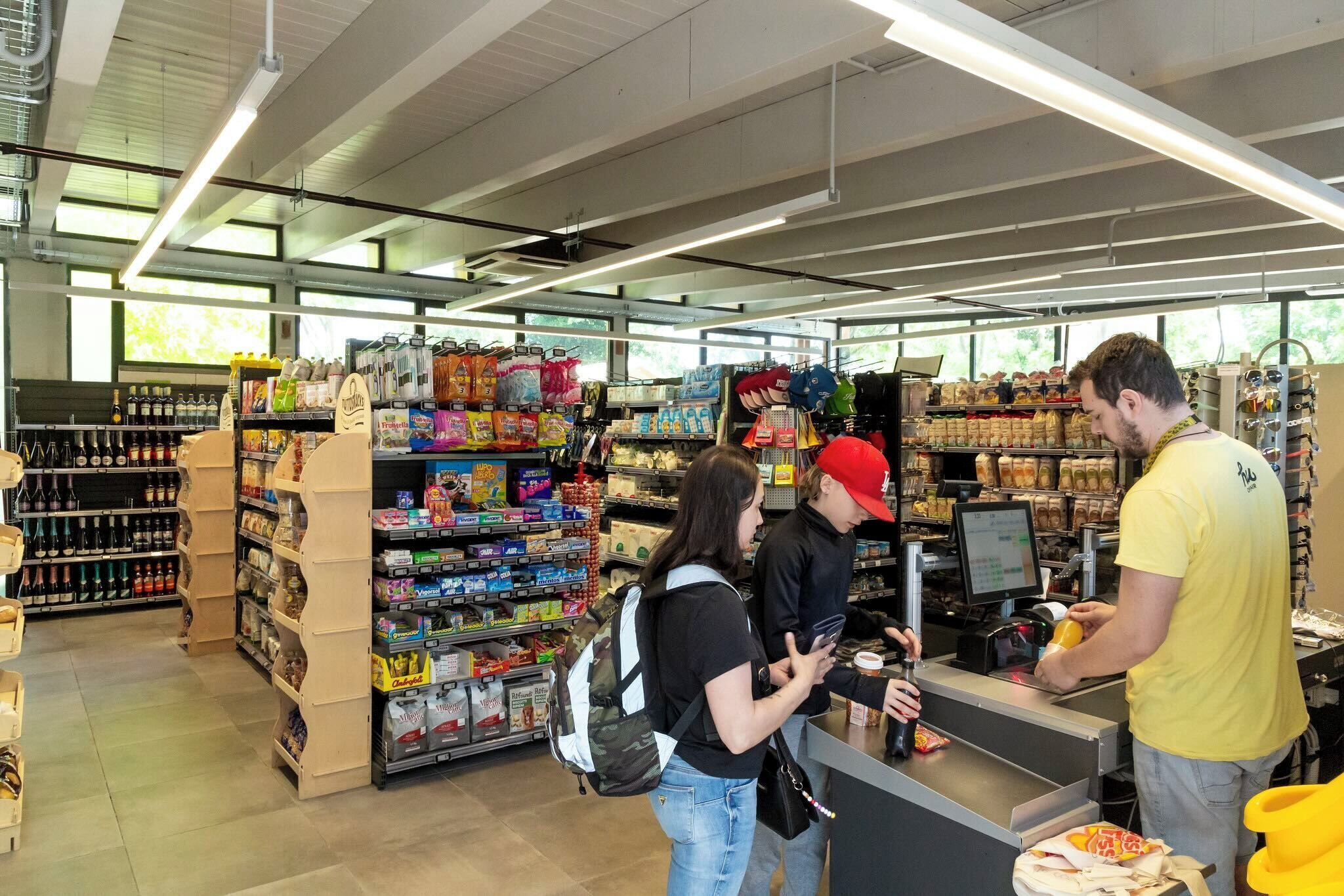 Interior de una tienda de comestibles con estantes llenos de diversos productos, una caja registradora y un cajero.