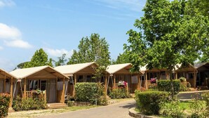 A row of wooden cabins with pitched roofs, surrounded by greenery and a clear sky.