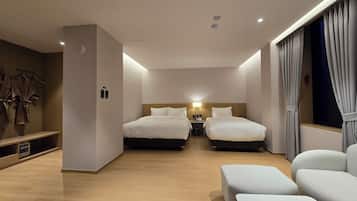 A hotel room with two beds, a desk, a chair, and a small seating area.