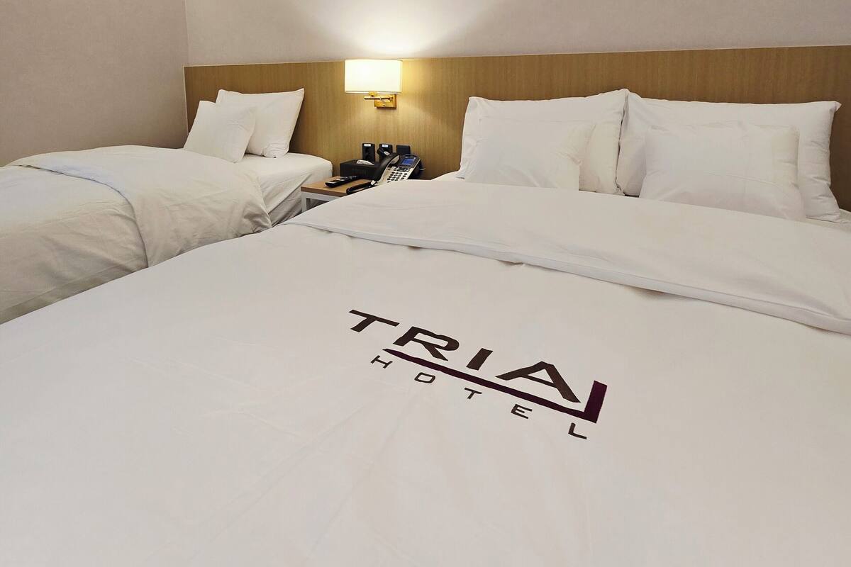 A TRIA HOTEL room with two beds, a bedside table with a lamp, and a phone.