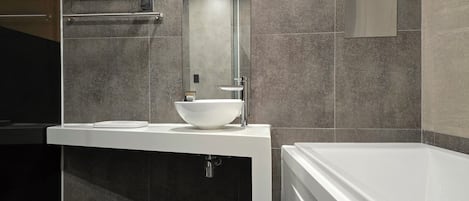 Un baño moderno con un lavamanos blanco, un espejo grande y una bañera.