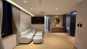 A modern hotel room with a sofa, a small table with a mirror, a flat-screen TV, and an elevator. - Tria Hotel (Seoul)