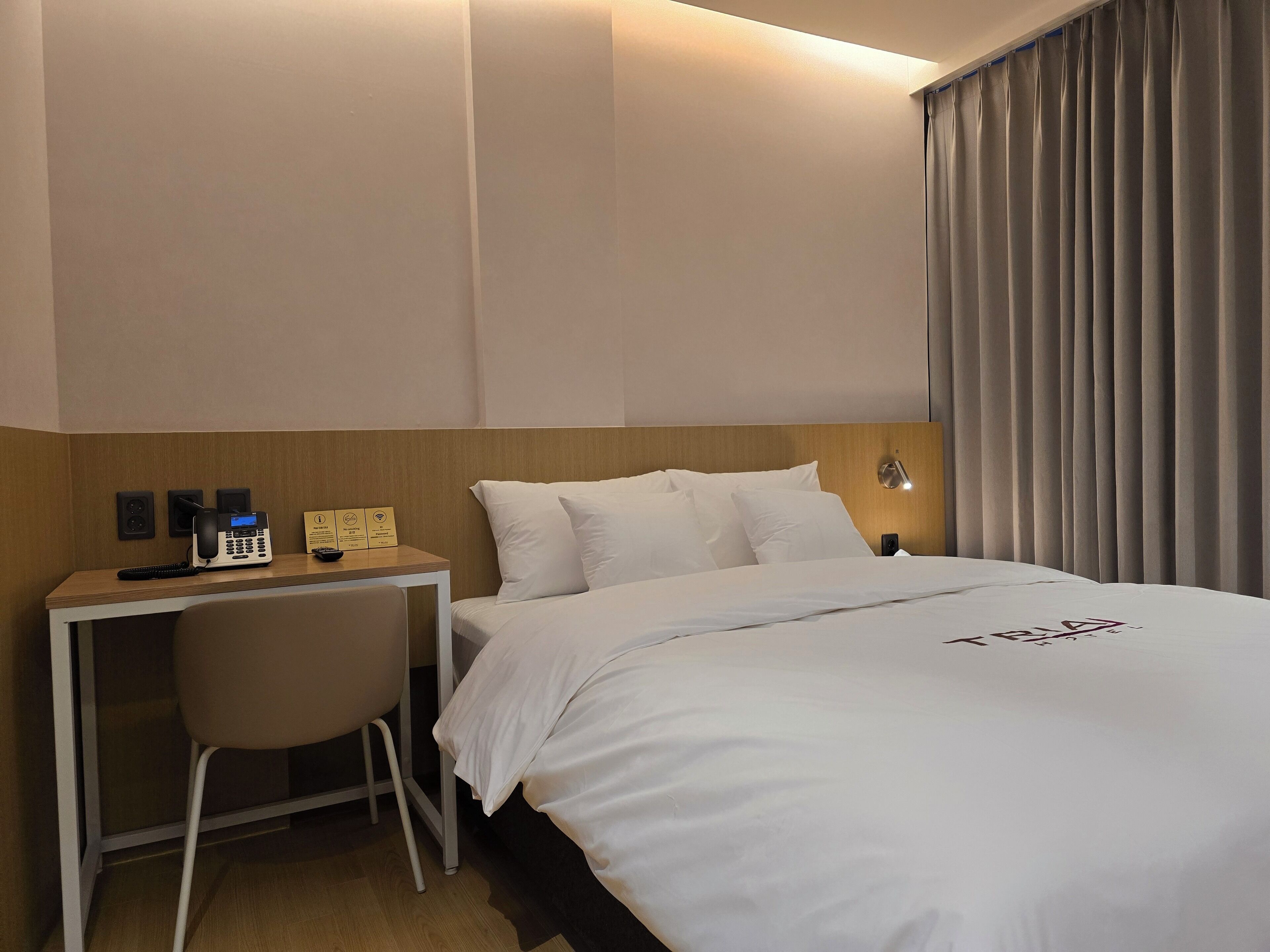 A hotel room with a bed, a desk with a phone, and a chair.