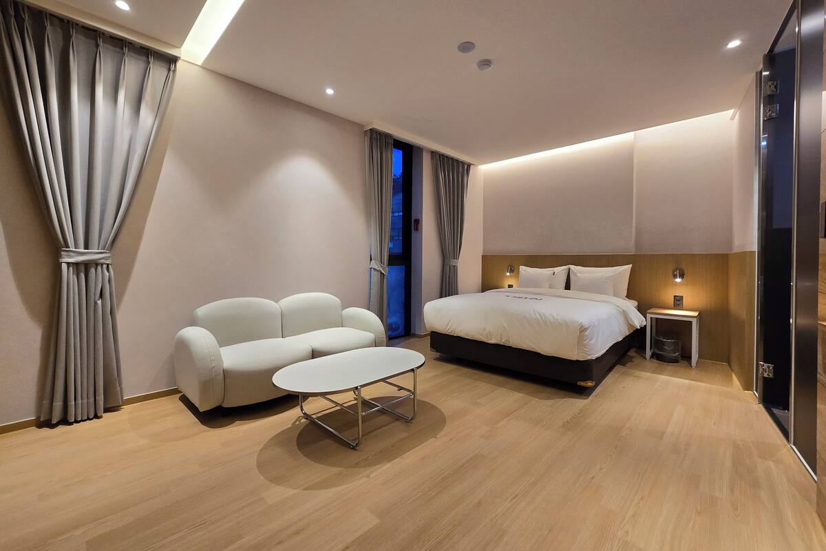 A modern bedroom with a bed, a sofa, a small table, and a nightstand.