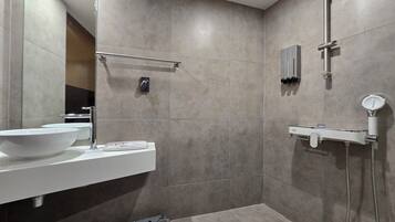 A modern bathroom with a large mirror, a white sink, a handheld showerhead, and a towel rack.