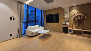 A modern hotel room with a large window, a flat-screen TV, a sofa, a small table, and a robe rack. - Tria Hotel (Seoul)