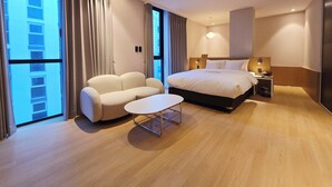 A modern hotel room with a large bed, a sofa, a small table, and a nightstand. - Tria Hotel (Seoul)