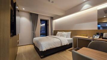 A modern hotel room with a bed, desk, chair, and a large window with curtains.
