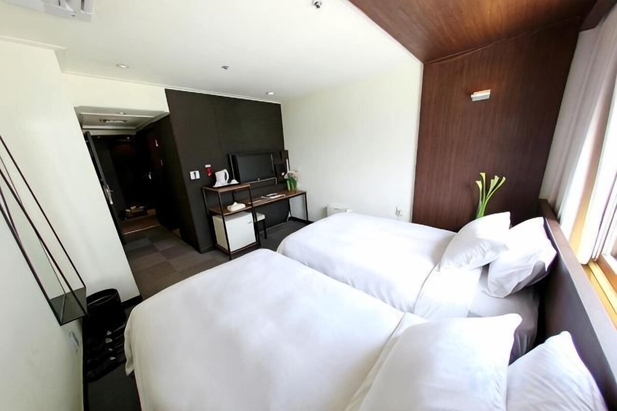 Habitación de hotel con dos camas, un escritorio, un televisor y una ventana con cortinas.