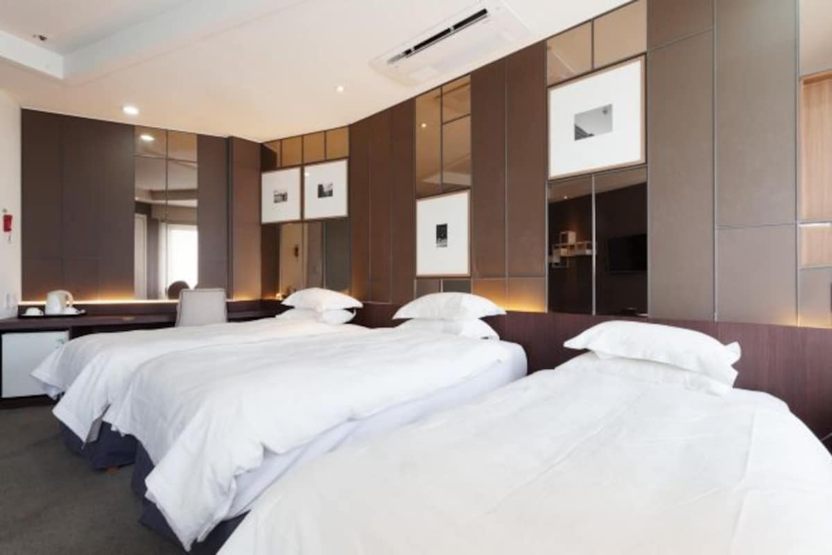 A hotel room with three single beds, a desk, and a large mirror.