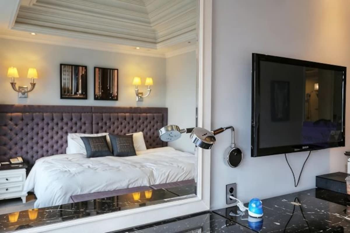 A modern hotel room with a large bed, a flat-screen TV, and a mirror.