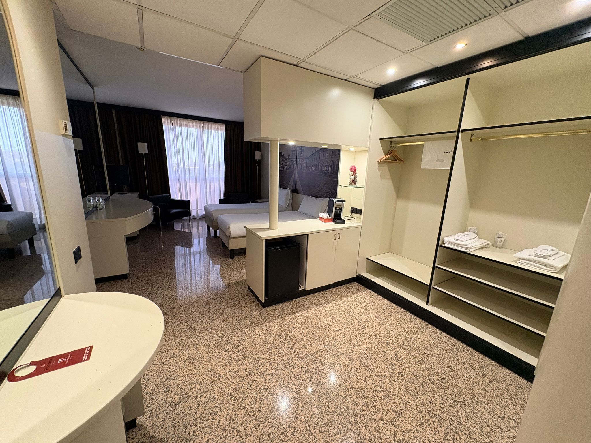 A modern hotel room with a bed, a desk, a mirror, a wardrobe, and a bathroom.