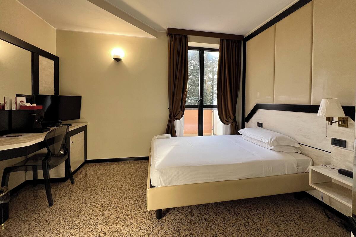 A hotel room with a bed, desk, chair, and a window with curtains.