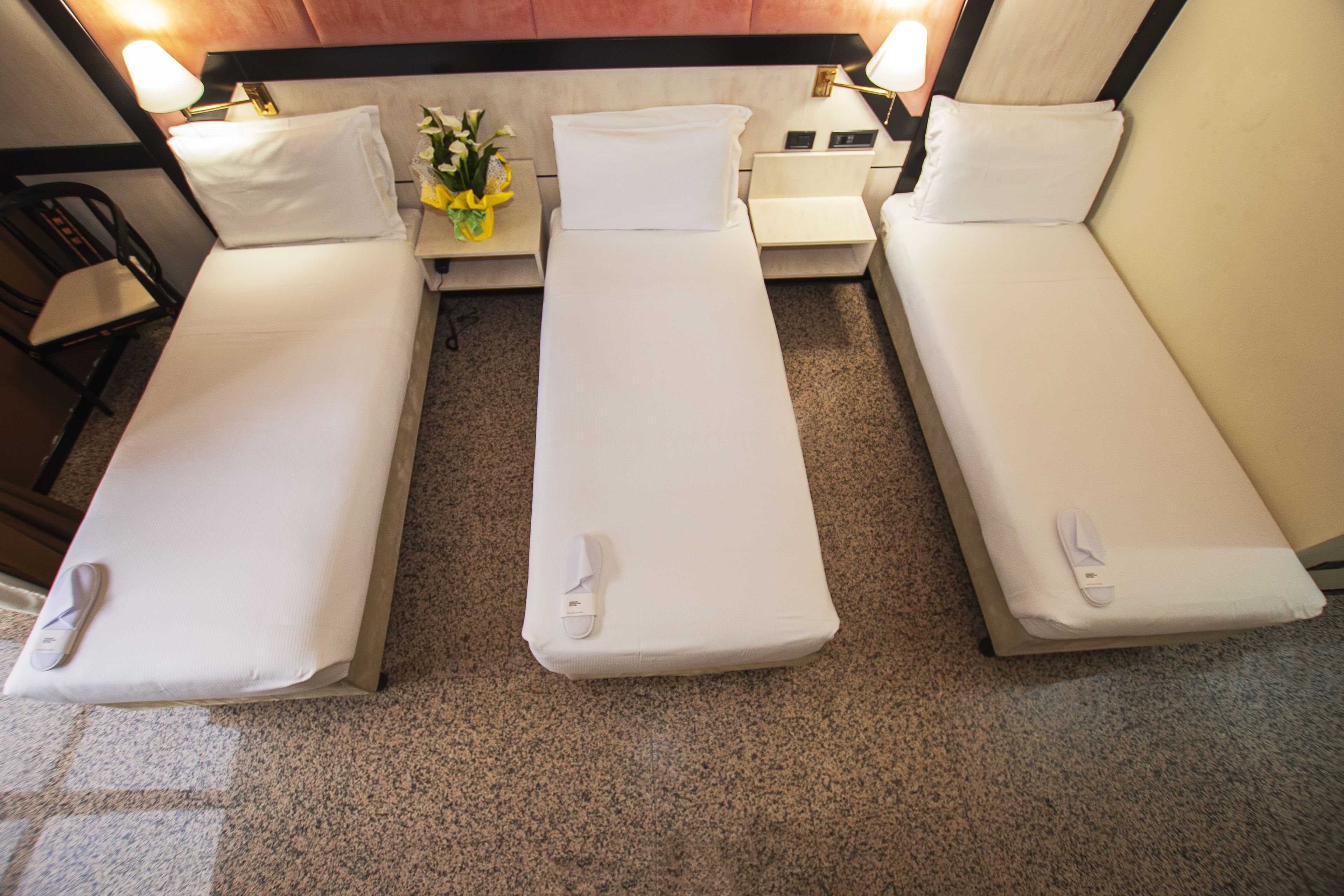 Ein Hotelzimmer mit zwei Einzelbetten, einem Nachttisch mit Lampe und einem kleinen Tisch mit Blumenvase.