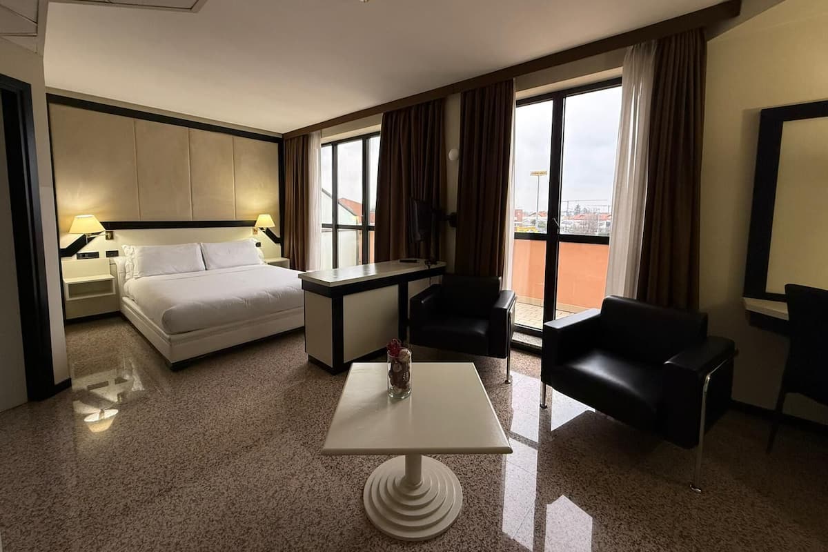 A hotel room with a bed, a desk, a chair, and a view of the city.