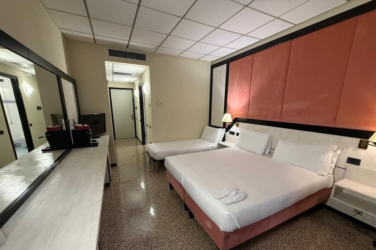 A hotel room with two beds, a large mirror, a desk with a chair, and a TV.