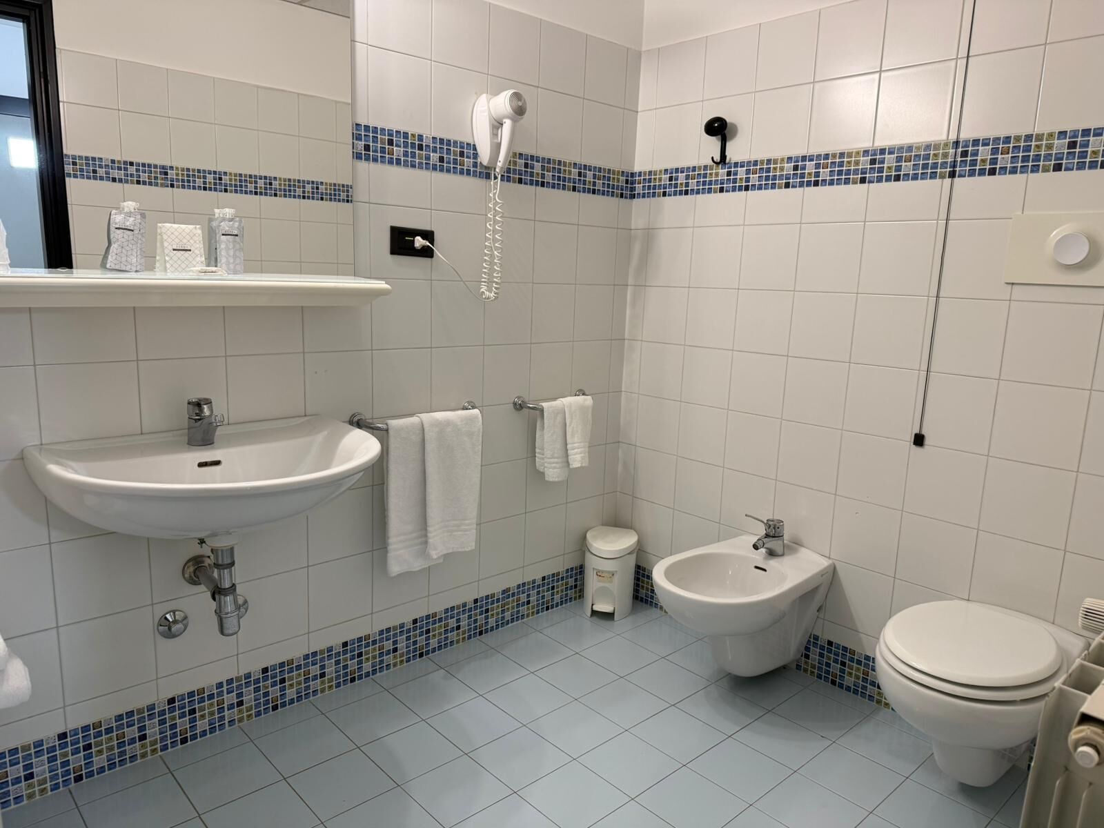 Une salle de bain équipée d’un lavabo, d’un bidet, de toilettes et d’un sèche-cheveux fixé au mur.