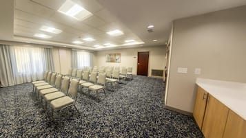 Un salón de conferencias con filas de sillas, piso alfombrado y una puerta al fondo.