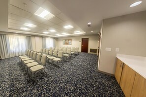 Una sala conferenze con file di sedie, pavimento rivestito di moquette e una porta sullo sfondo.