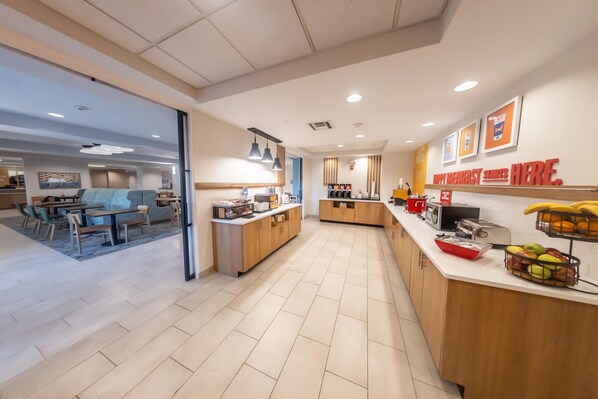 A modern kitchen area with a breakfast bar, a seating area with tables and chairs, and a counter with fruits and a coffee machine. - Hampton Inn Winfield (Winfield)