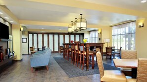 A hotel dining area with a long table, multiple chairs, a sofa, and a television on the left.
