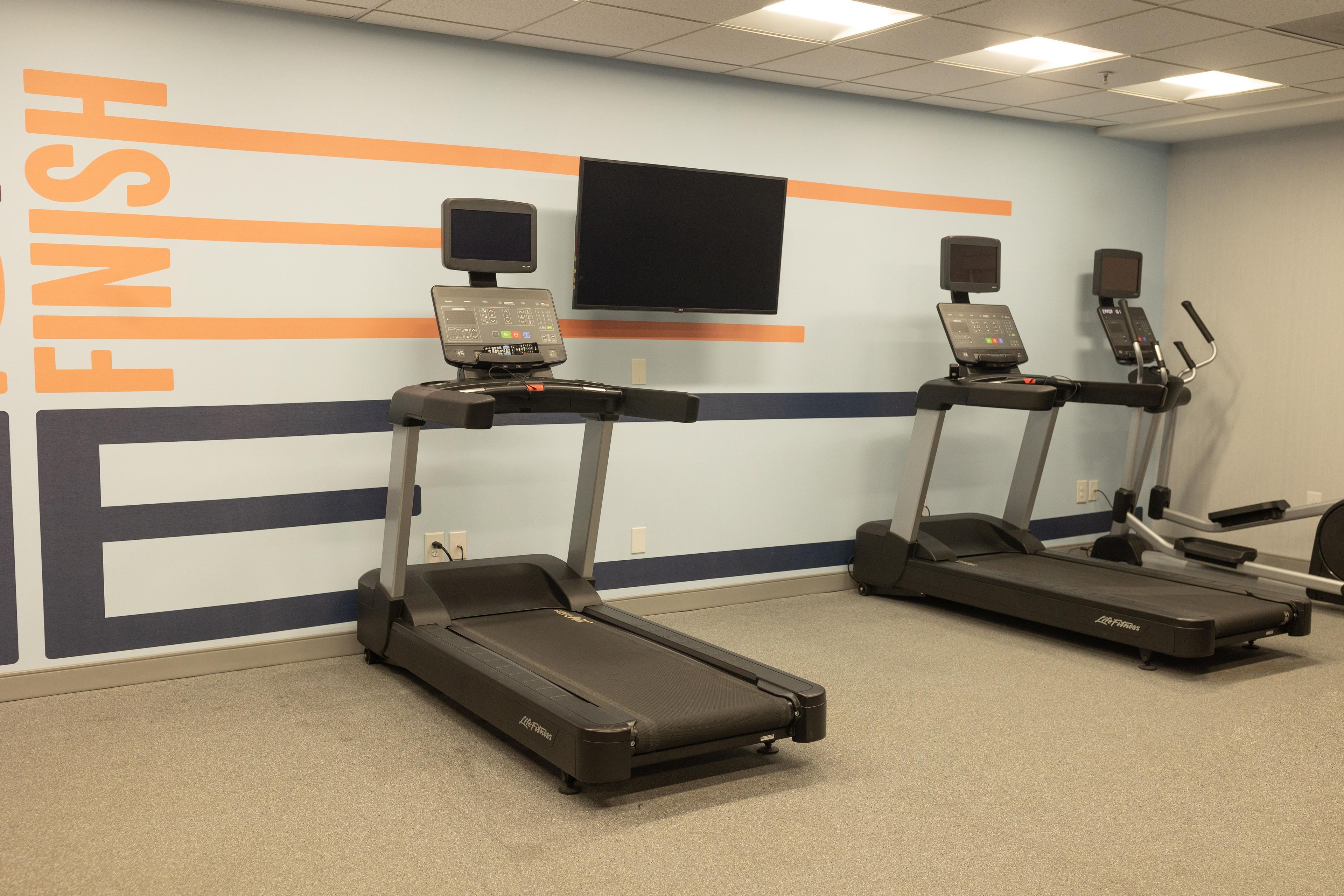 A fitness room with two treadmills, a wall-mounted TV, and a motivational 'FINISH' sign.