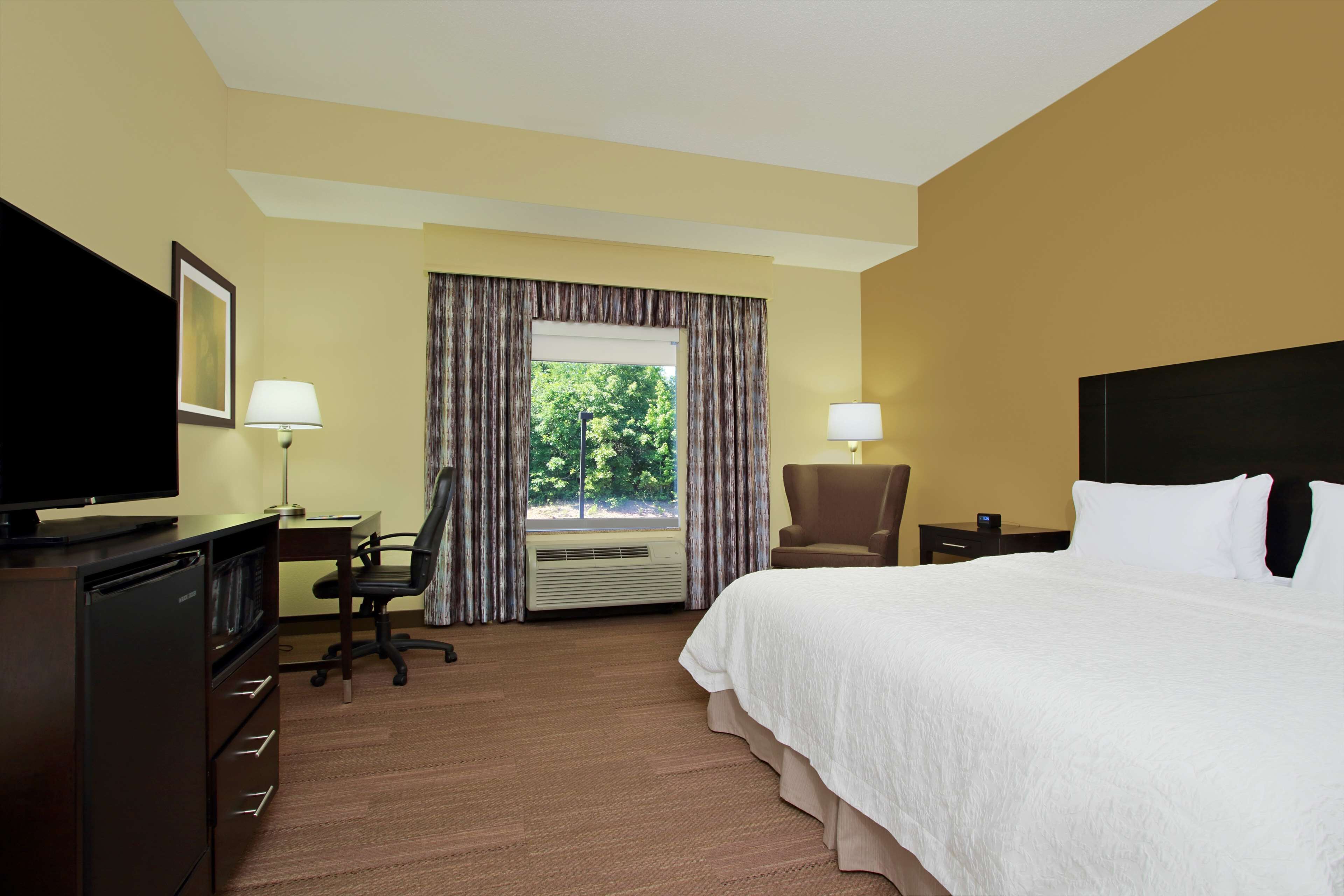 A hotel room with a large bed, a desk with a chair, a television, and a window with curtains.