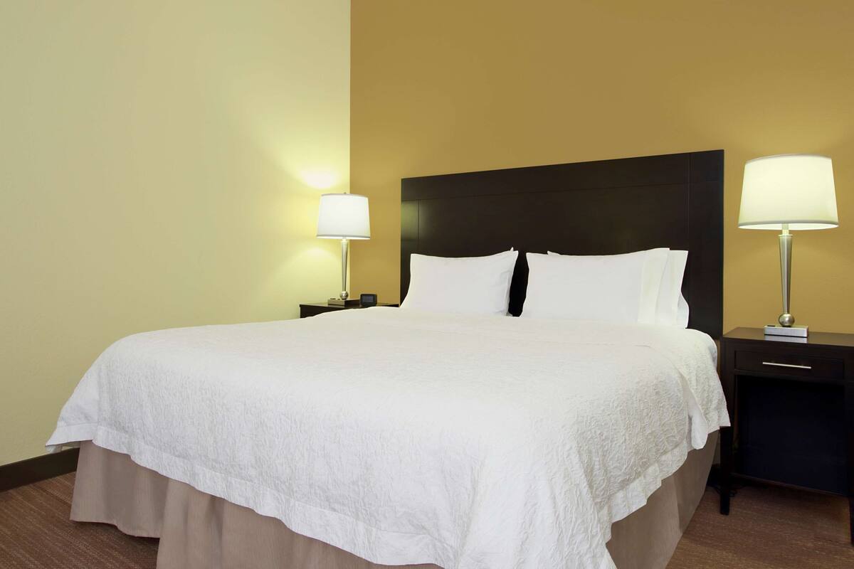 Una habitación de hotel con una cama grande, dos mesitas de noche con lámparas y un tocador con lámpara.