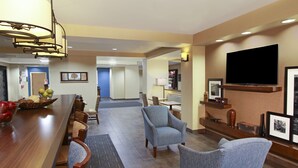 Un hall de hotel con un largo mostrador de recepción de madera, un televisor montado en la pared y una zona de estar con dos sillones y un sofá.