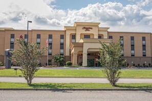 Un hotel Hampton Inn con fachada moderna, una entrada central y un césped bien cuidado.