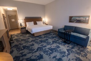 A hotel room with a bed, a blue sofa, a desk, and a painting on the wall. - Hampton Inn Winfield (Winfield)