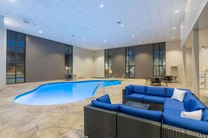 An indoor swimming pool with a blue interior, surrounded by a seating area with blue cushions and wicker furniture.