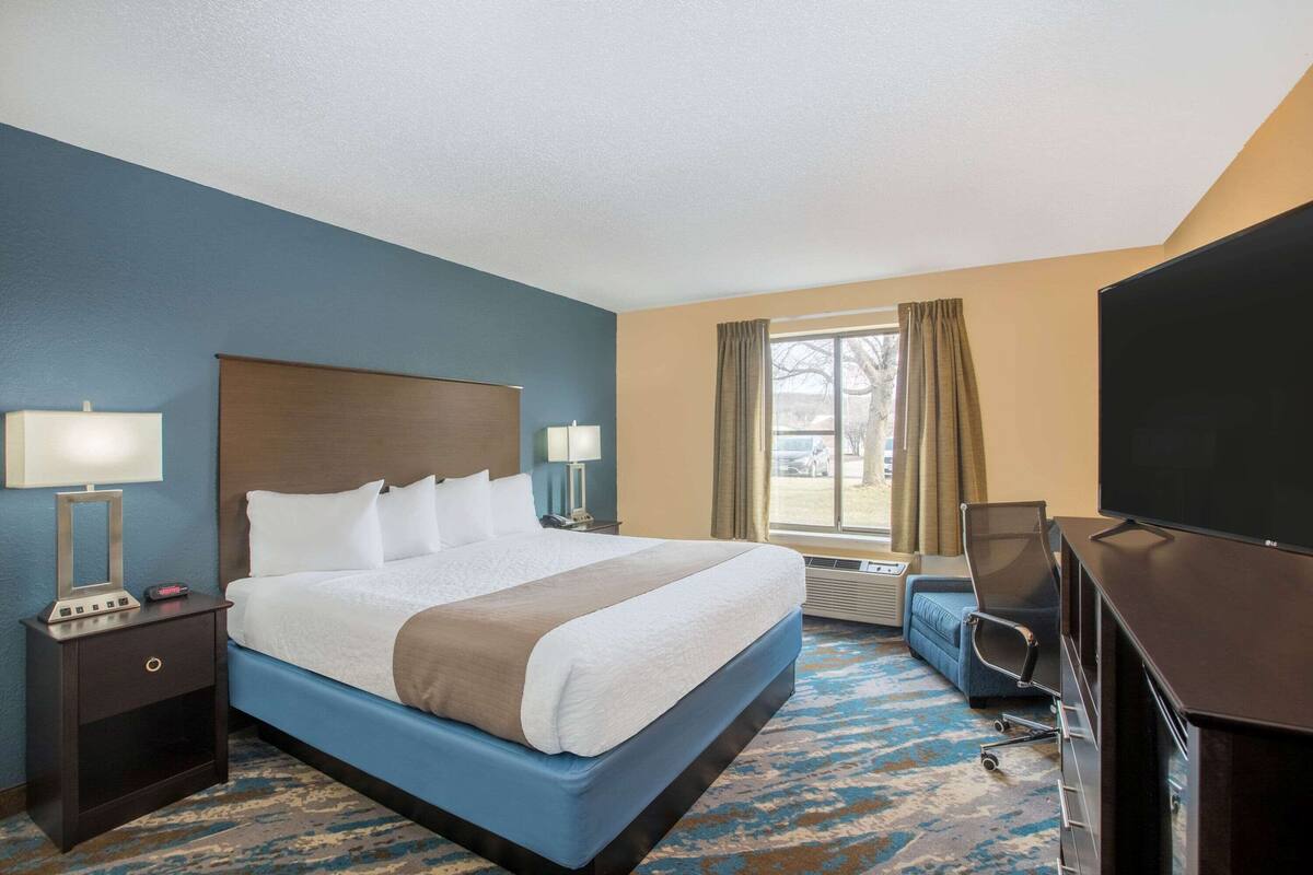 Una habitación de hotel con una cama grande, mesitas de noche con lámparas, un escritorio con silla, un televisor y una ventana con cortinas.