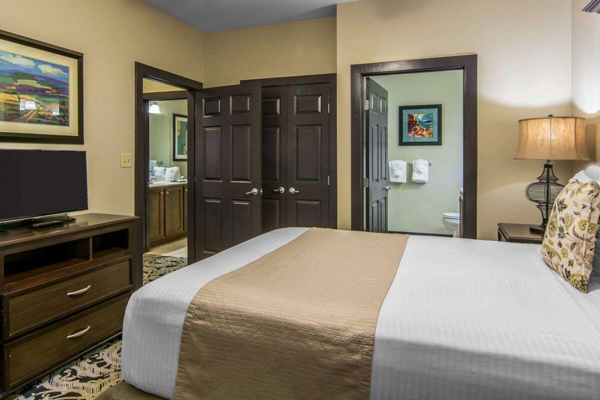 Una habitación de hotel con cama, televisión, escritorio, lámpara y ventilador de techo.