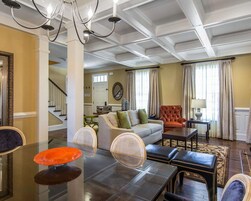 Una sala de estar amplia con techo alto, un comedor con mesa de vidrio y una escalera que lleva a otro nivel.