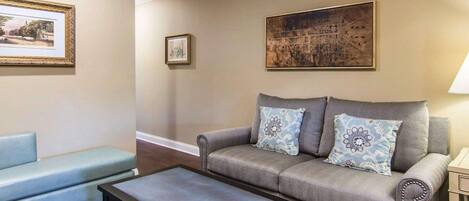 A living room with a grey sofa, a blue armchair, and a black coffee table. There are two framed pictures on the wall and a lamp on the right.