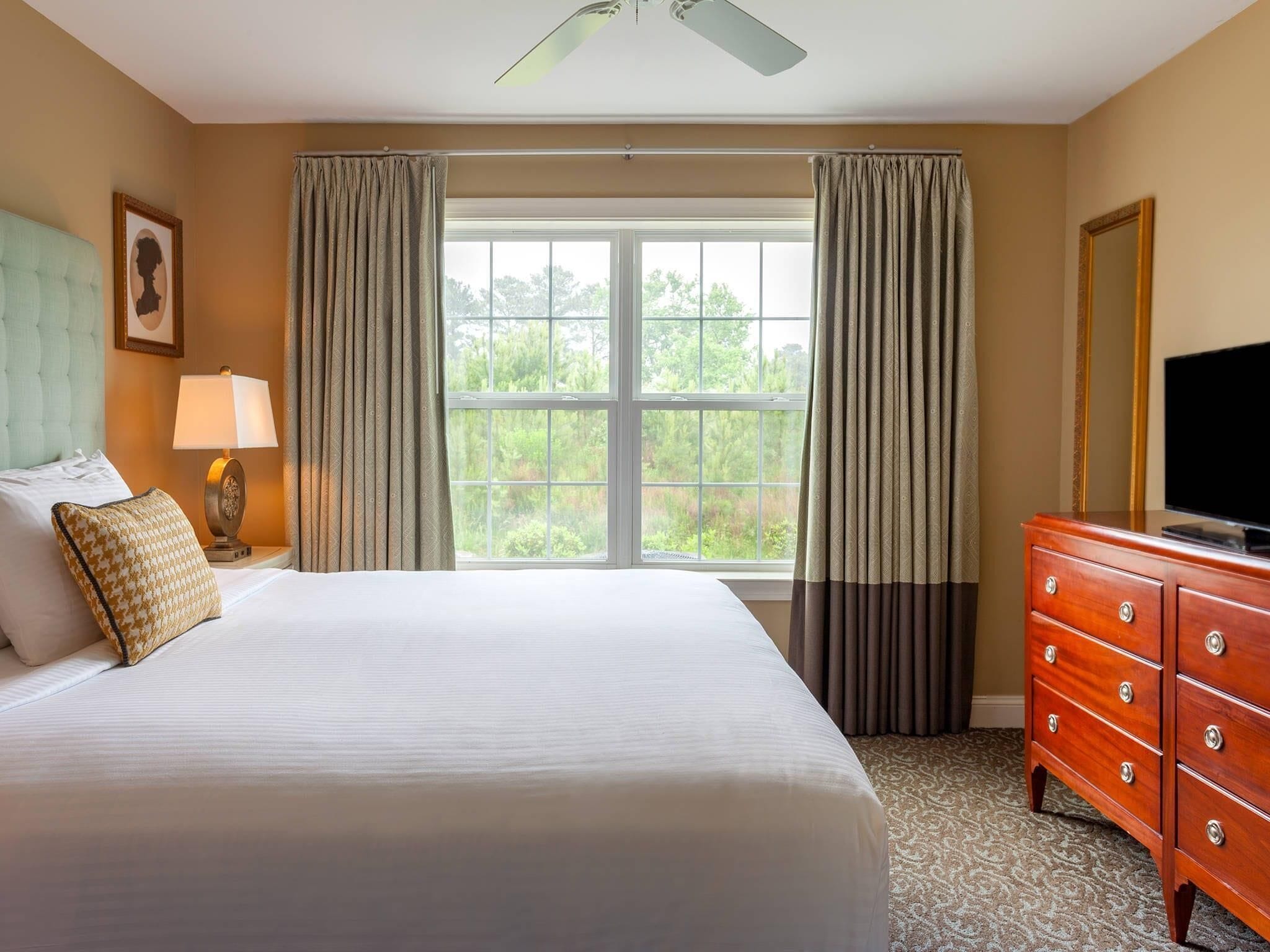 A hotel room with a large bed, a dresser, a television, and a window with curtains.