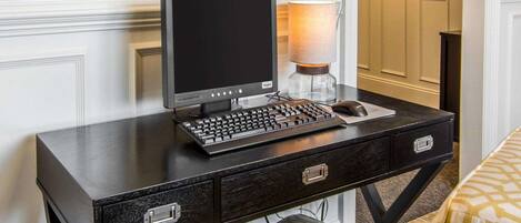 Een hotelkamer met een donker houten bureau, een computer, een lamp en een gestreept kussen.