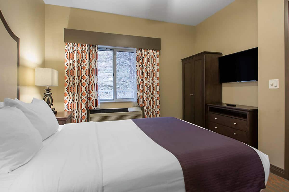 A hotel room with a large bed, a TV mounted on the wall, a wardrobe, and a window with patterned curtains.