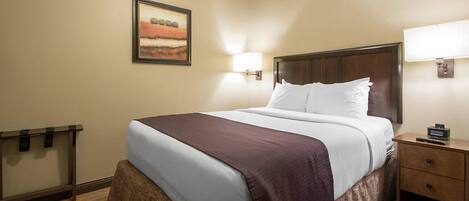 A hotel room with a bed, a nightstand, a lamp, and a painting on the wall.
